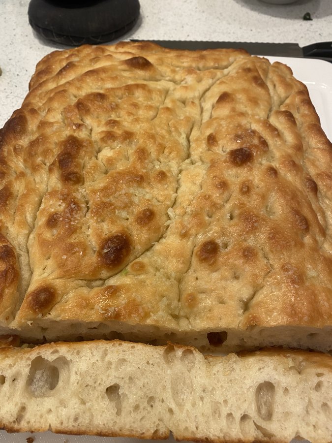 A tray of focaccia with a dimpled golden top, one slice cut to show the crumb